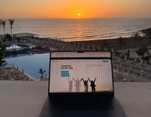 laptop met op de achtergrond de zee en ondergaande zon