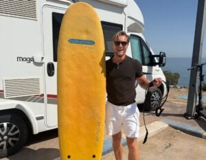 Henno with his surfboard and RV by the sea